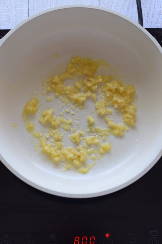 Cooking garlic in a white skillet.