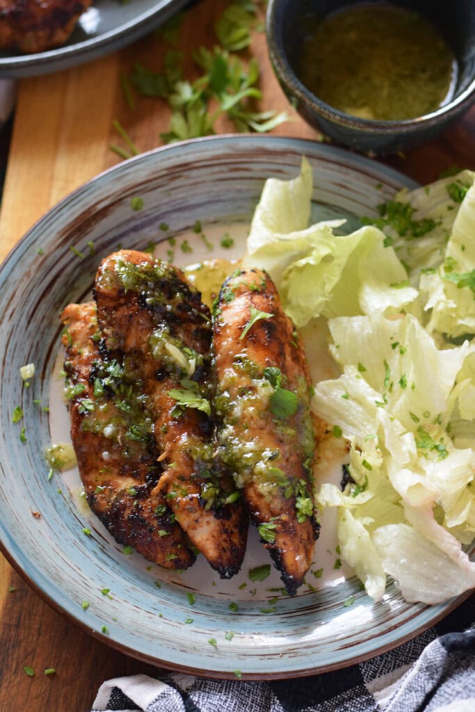 Honey dijon chicken tenders on a blue plate with lettuce leaves.