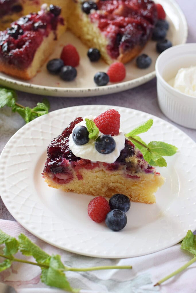 A slice of berry cake on a plate with whipped cream.