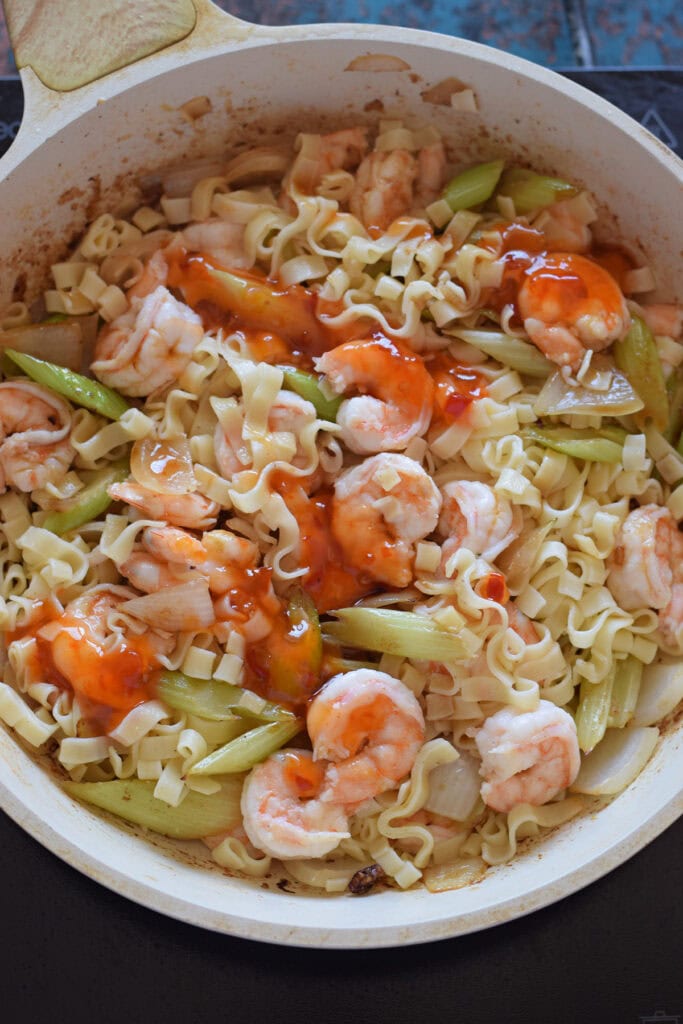 Adding sauces to a skillet with noodles and shrimp.