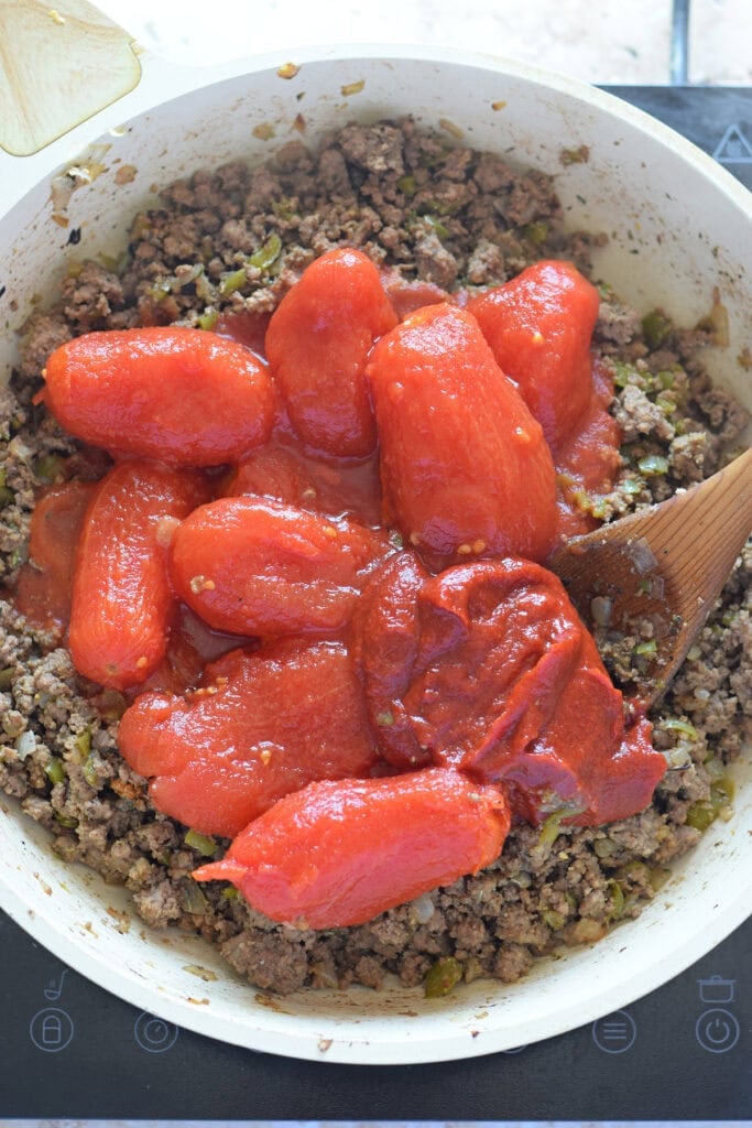 Adding canned tomatoes to ground beef.