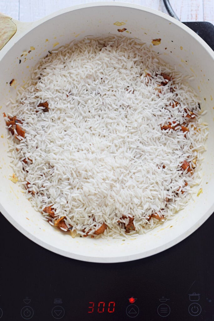 Adding rice to a skillet with sun dried tomatoes and onions.