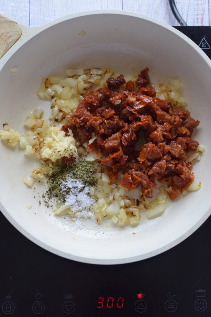 Adding sun dried tomatoes and herbs to a skillet.