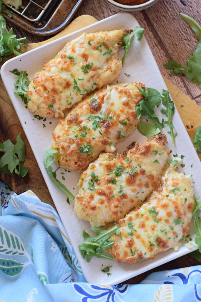 Mozzarella crusted chicken on a white serving dish.