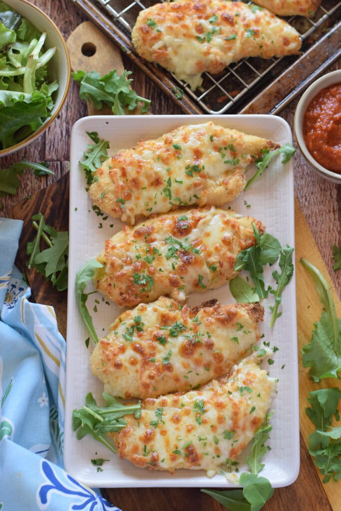 Mozzarella baked chicken on a white serving plate.