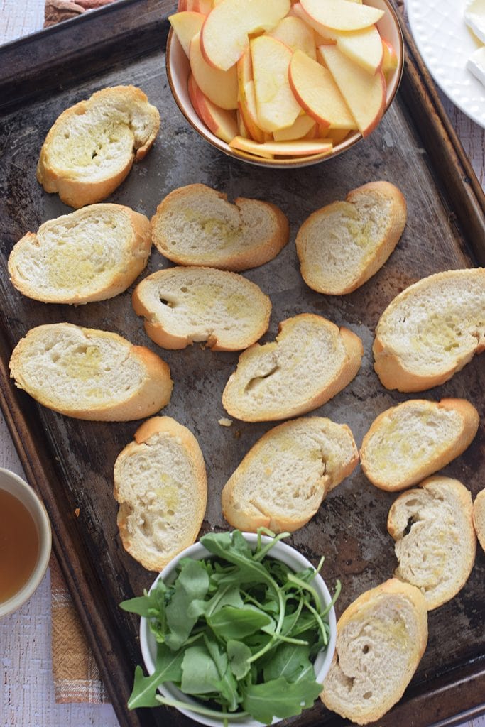 Bread on a baking tray with apple slices and arugula leaves.