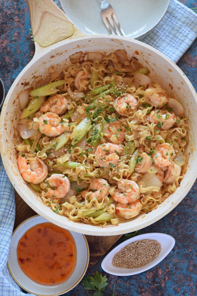Shrimp and noodle stir fry in a white skillet.