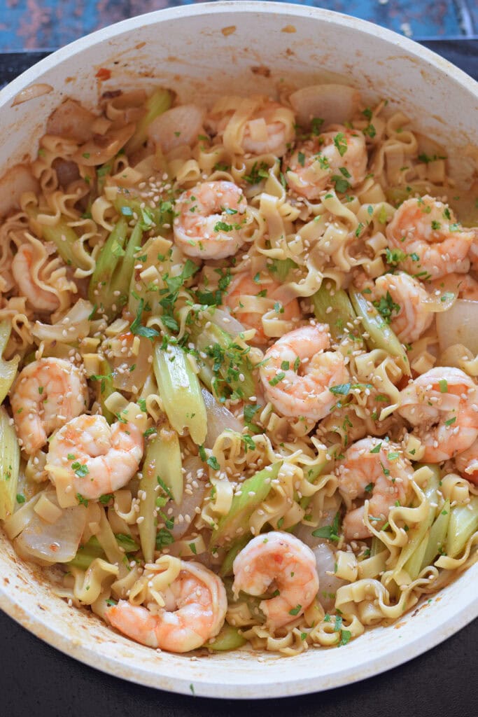 Shrimp and noodle stir fry in a white skillet.