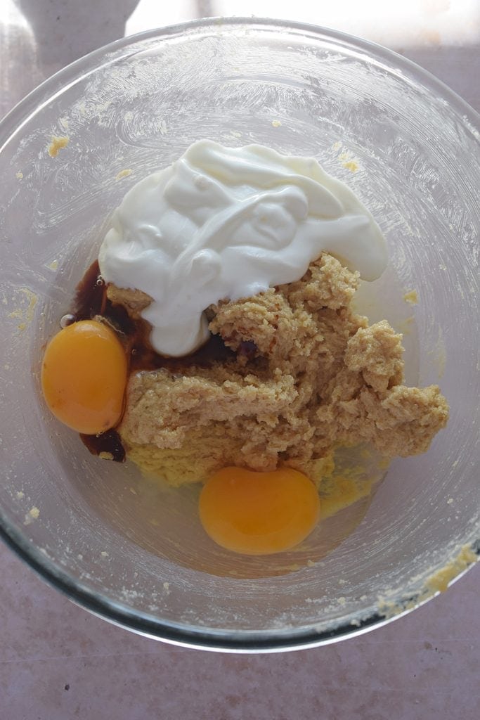 Adding eggs and yogurt to muffin batter in a glass bowl.
