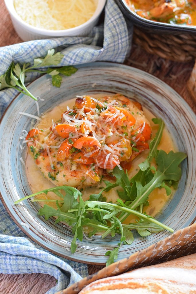 Chicken on a plate with tomato, arugula and parmesan cheese.