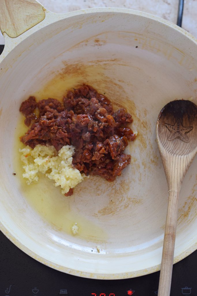 Adding sun dried tomatoes and garlic to a skillet.
